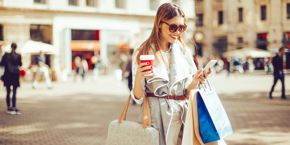 mulher com sacolas de compras, smartphone e café nas mãos